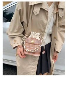 Detail of pink woven bucket bag with pearl accents and white chain worn with a trench coat