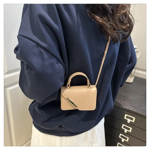 Mini sac bandoulière beige en similicuir avec barre dorée porté par un mannequin