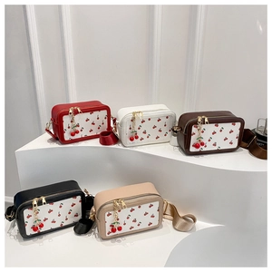 Detail view of five cherry-patterned leather crossbody camera bags in various colors