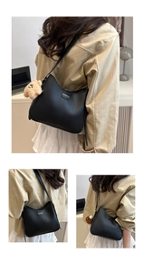 Detail of black matte leather shoulder bag with gold metal logo and brown teddy bear charm