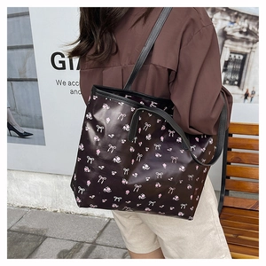 Gros plan du sac cabas noir avec fleurs roses et nœuds blancs sur un banc en bois