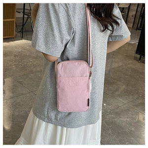 Pink nylon crossbody phone bag shown with adjustable strap and front pocket on person