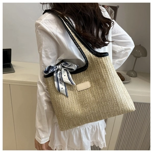 Detalle del bolso tote de paja tejida con ribete de cuero negro y accesorio de pañuelo de seda