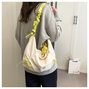Détail du sac en nylon crème avec bandoulière plissée verte et charm floral amovible