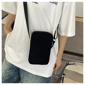 Model wearing a minimalist black canvas mini crossbody phone bag with front pocket and zipper