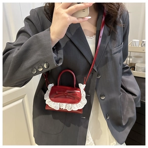 Mini red patent leather handbag with lace trim and bow detail shown in a mirror selfie