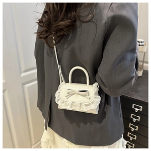 Mini white leather handbag with lace trim and bow detail shown on a model