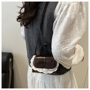 Détail d'un mini sac en cuir verni marron avec bordure en dentelle et nœud porté en bandoulière