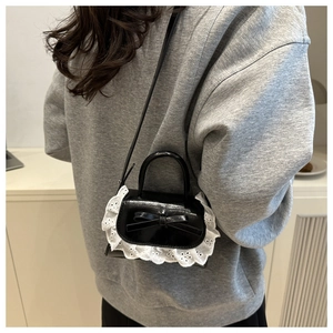 Detail van mini crossbodytas met witte kantafwerking, zwart glanzend leer en een strik