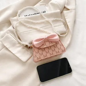 Detail of pink mini bag with bow, pearl chain and M-letter print on beige blazer background