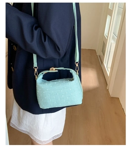 Detail der mintgrünen Stoffhandtasche mit Goldbeschlägen auf blauem Blazer