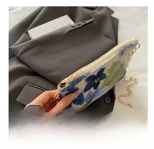 Detail of floral embroidery and sequins on creamy clutch bag with gold zipper