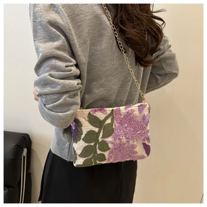 Detail of sequined floral knit crossbody bag with golden chain on grey sweater