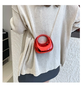 Detail of red glossy mini hobo bag with gold chain strap on beige knitwear