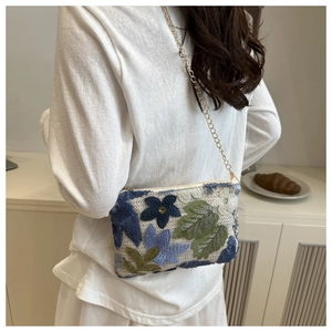 Detail of floral embroidery and sequins on the off-white chain bag with a gold strap