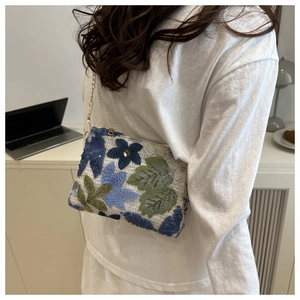 Detail of embroidered floral handbag with golden chain strap on a cream knit texture