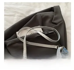 Detail of blue denim mini bag with silver floral charm and pearl accent on grey blazer