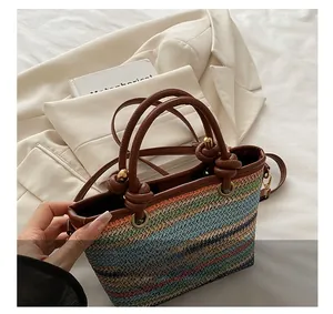 Détail d'un sac en paille tissée à rayures colorées avec anses en cuir marron et nœuds