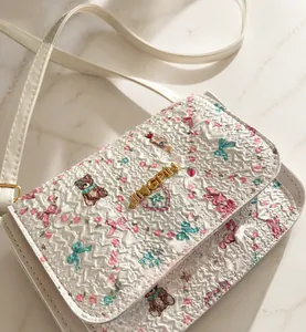 Détail du sac bandoulière blanc imprimé avec motifs floraux et logo en métal doré
