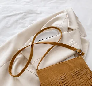 Detail of brown suede crossbody bag featuring fringe decor and adjustable strap on a blazer