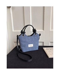 Dettaglio della borsa a tracolla in denim blu con manici annodati neri e logo patch
