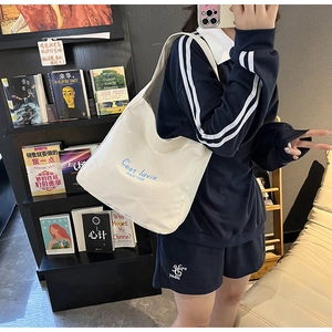 Détail du sac cabas en toile blanc cassé avec texte artistique bleu et bandoulière chic