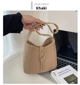 Close-up of khaki bucket bag with white stitching, gold ring detail and fringe tassels