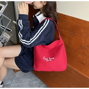 Detail view of red canvas tote bag with C'est la vie slogan worn by model in casual style