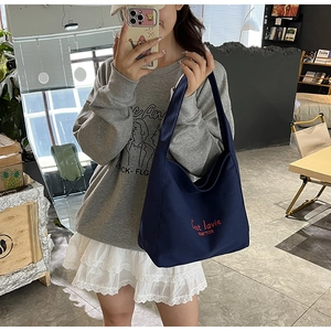 Sac fourre-tout en toile bleu marine avec broderie rouge présenté dans un cadre décontracté