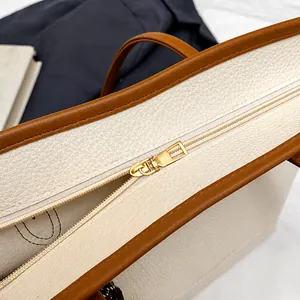 Detail of cream tote bag featuring brown leather trim and a premium gold zipper closure