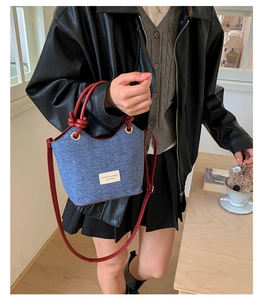 Dettaglio della borsa a secchiello in denim blu scuro con tracolla in pelle rosso acceso