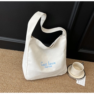 Détail du sac cabas en toile blanche avec lettrage bleu sur tapis marron