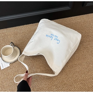 Gros plan du sac cabas en toile crème avec imprimé bleu C'est la vie sur fond texturé