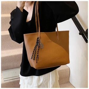 Detailed view of brown textured tote bag with metal tennis racket charm and leather strap