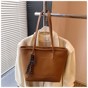 Detail of caramel brown lychee leather tote bag with FASHION emboss and tennis racket charm