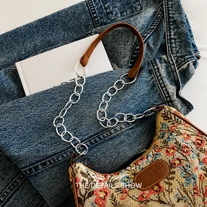 Detalle de bolso jacquard floral con cadena plateada sobre fondo de tela vaquera