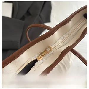 Close-up of smooth light gold zipper detail on a cream textured faux leather tote bag