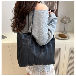 Detailed view of black textured tote bag with vertical wave pattern and leather straps