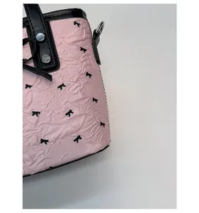 Détail du sac en tissu plissé rose avec imprimé nœud noir et rivets métalliques