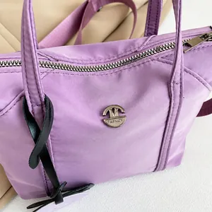 Detailaufnahme der lila Nylontasche mit silbernem Reißverschluss und modischem Logo-Schild