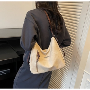 Detail of beige suede hobo bag featuring adjustable brown strap and metal fashion logo