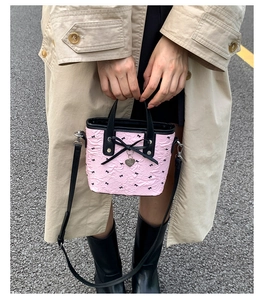 Détail du sac seau texturé rose clair avec des nœuds noirs et un pendentif en cœur
