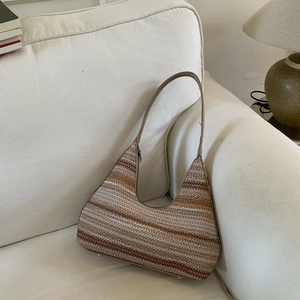 Detail of a striped knit bucket bag with metallic base studs on a cream fabric sofa