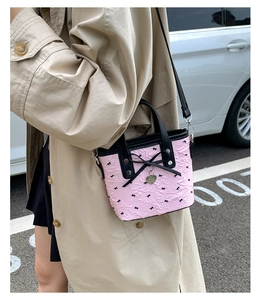 Sac seau plissé rose avec nœud noir et pendentif cœur porté sur un manteau beige