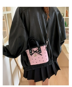 Détail du sac seau rose à nœuds avec pendentif cœur porté par un mannequin chic