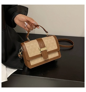 Close-up of beige geometric embossed handbag with brown leather trim and golden hardware
