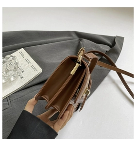 Detail view of brown leather bag with triple compartments and gold twist lock closure