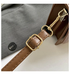 Close-up of golden metal buckle and stitching details on a brown leather handbag