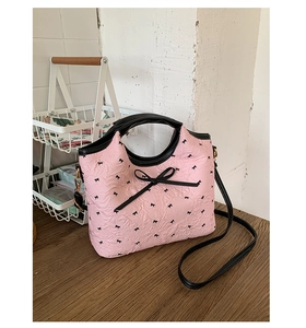 Vista de detalle del bolso tipo cubo rosa con lazos negros y textura de cuero plisado
