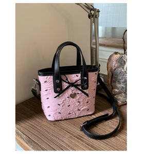Detalle del bolso saco plisado rosa con lazos negros y colgante de corazón plateado
